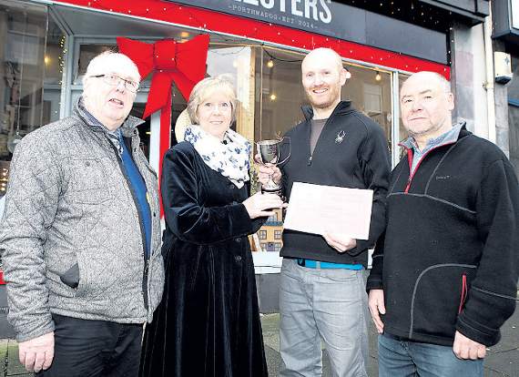 The winner of the Porthmadog Christmas Window competition for businesses was Glosters. Pictured is Tom Gloster receiving his prize from judges Angela and Bill Swann and Cllr Selwyn Griffiths
