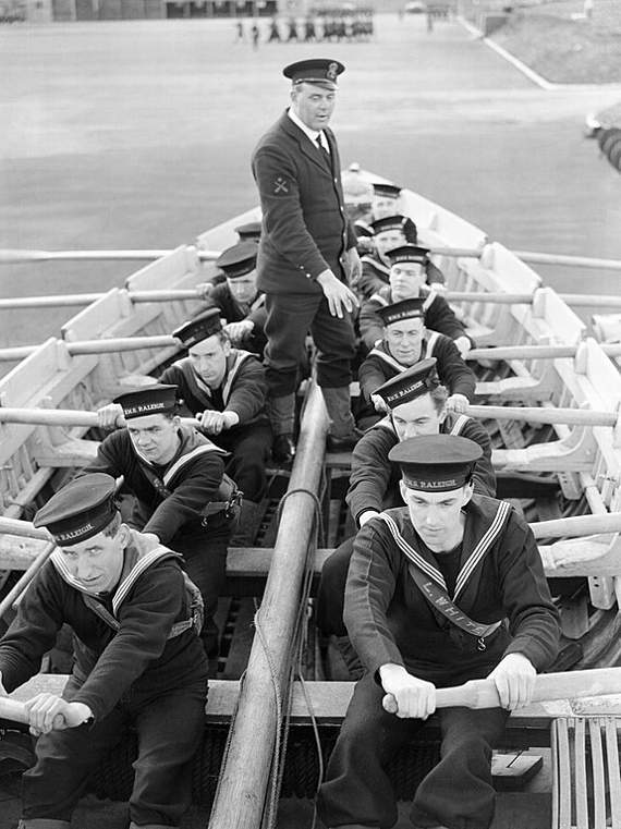 At HMS Raleigh in 1941, new recruits to the Navy learn to row a boat on dry land, preparatory to instruction on nearby water. Source Imperia War Museum collection