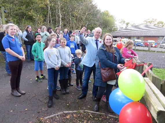 Crediton Hamlets Parish Council vice chairman John Stevens waves the scissors before cutting the sparkling red ribbon across the entrance to the new play park at Yeoford. Holding the bow is Tabitha Maynard, watched by a few of the children who rushed in as soon as it was open. SR 1645