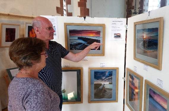 Photographer Andy Wills is showing his work to a visitor at the St Lawrence Chapel venue with artists John Lewis, John Sellings and Tim Salter.