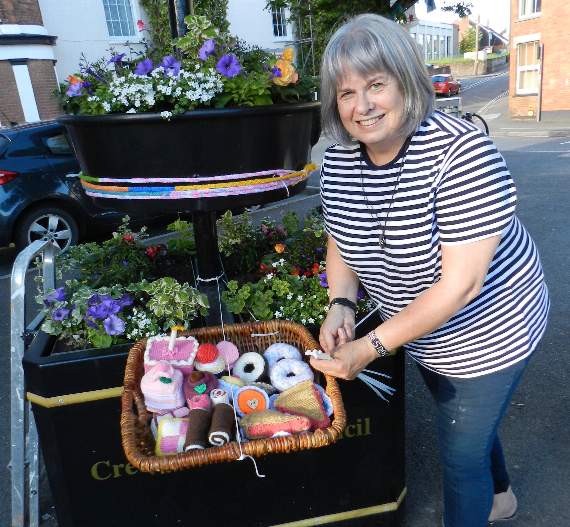 Crediton Foodbank Co-ordinator and Community Support Worker, Chris Parsons, with a basket of knitted cakes during the Christians in Crediton’s yarn bombing of the Town Square. NP 310519 01