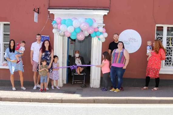 Cllr Frank Letch, the Mayor of Crediton, seated centre, cuts the ribbon to officially open Crediton Baby Hub, with Jess and her husband, left. AQ 8432