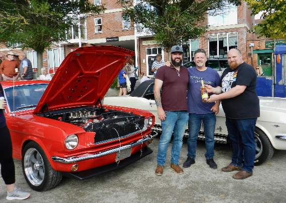 Organiser, Dan Webb (right) with Steven and Kevin Cox beside the Red Mustang 65 that was awarded ‘Best in Show’ at the recent Cars and Coffee event. NP 091021 06