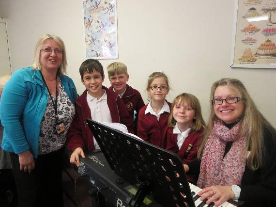 Children from St Lawrence Primary School and their teacher sing to music played by pianist Pam Edwards, a director of Home Instead