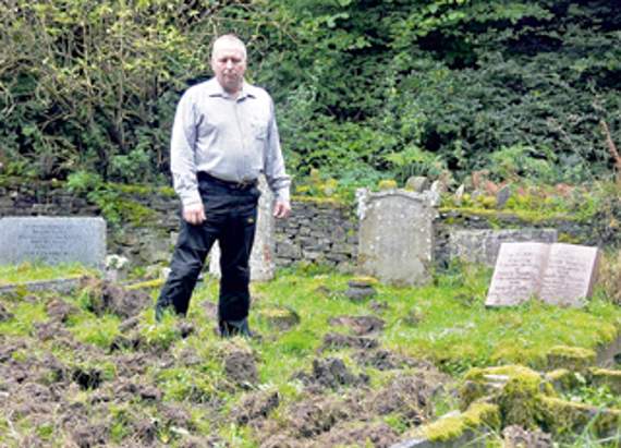 •Cllr Alan Grant looks at the damage caused by wild boar in the graveyard at St Paul’s Church last Friday.
