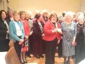 Members of the club watching president Evelyn presenting the cheque to District chairman Karen.
