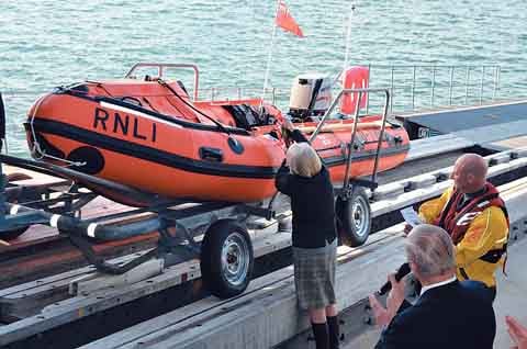 Mrs. Frances Coward gives RNLI Angle’s new inshore lifeboat a champagne send-off watched by lifeboat operations manager John Allen-Mirehouse and helmsman Adam Stringer.