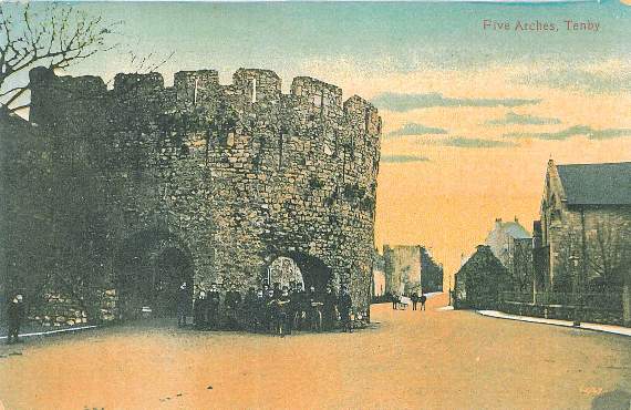 For the postcard on the left, Valentine’s have tinted an old photograph showing boys with bicycles gathered near the Five Arches. One boy stands near the wall in the foreground, with three more set back some distance. One of them has a hand cart for deliveries.