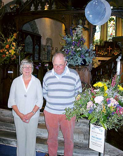 David and Pat Henderson, two of the organisers of the festival at St. James’ Church, stand alongside a floral tribute in loving memory of the late Mrs. Pat Crisp. Observer pic.