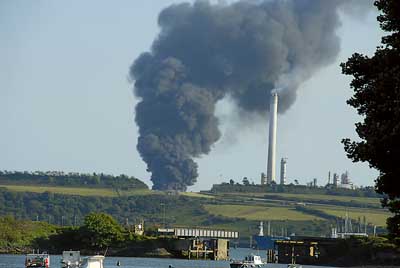 This photograph was taken a few minutes after the explosion occurred at the Chevron Oil Refinery at Pembroke. It was taken from Castle Pill, Milford Haven, by Sue Brindley and shows the huge plume of black smoke billowing into the early evening sky.