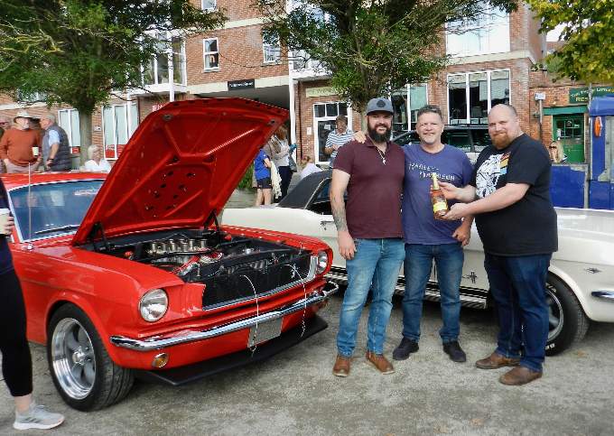 Organiser Dan Webb (right) with Steven and Kevin Cox beside the Red Mustang 65 which was awarded ‘Best in Show’ at the second Cars and Coffee event. NP 091021 06