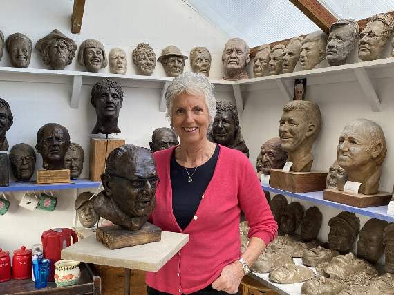 Penny Lally with her bust of Captain Sir Tom Moore, watched over by many of the other faces she’s captured in clay