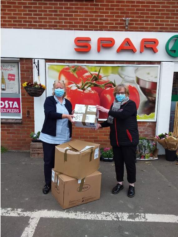 SPAR store owner Barbara Clements hands PPE parcel to Marie Curie Healthcare Assistant Liz Marshall