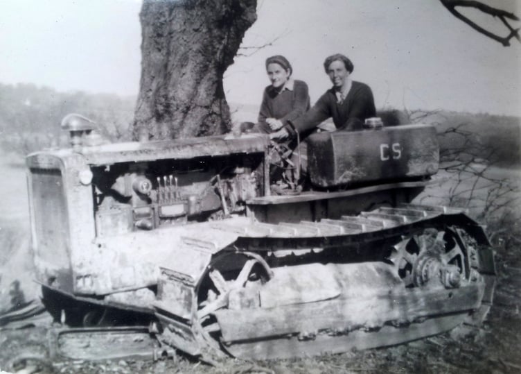 Joyce Elizabeth Gaster (left) driving a caterpillar tractor at Alice Holt Forest and, below, with corps members