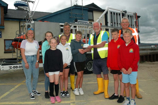 Aberdyfi Lifeboat Station chairman Dave Williams, launch authority and tractor drivers Huw Jones Williams and Josh Cooper, and lifeboat crew member and classroom assistant Abi Hinton receive a cheque from Ysgol Penybryn pupils