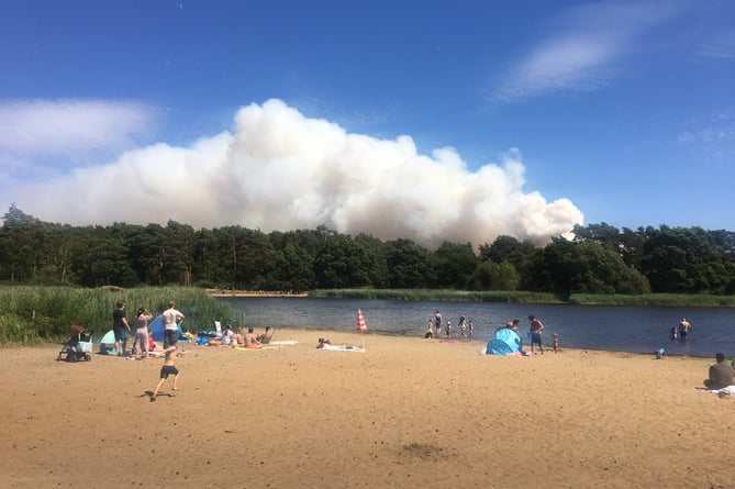 Onlookers watch a plume of smoke rising above Hankley Common from nearby Frensham Little Pond