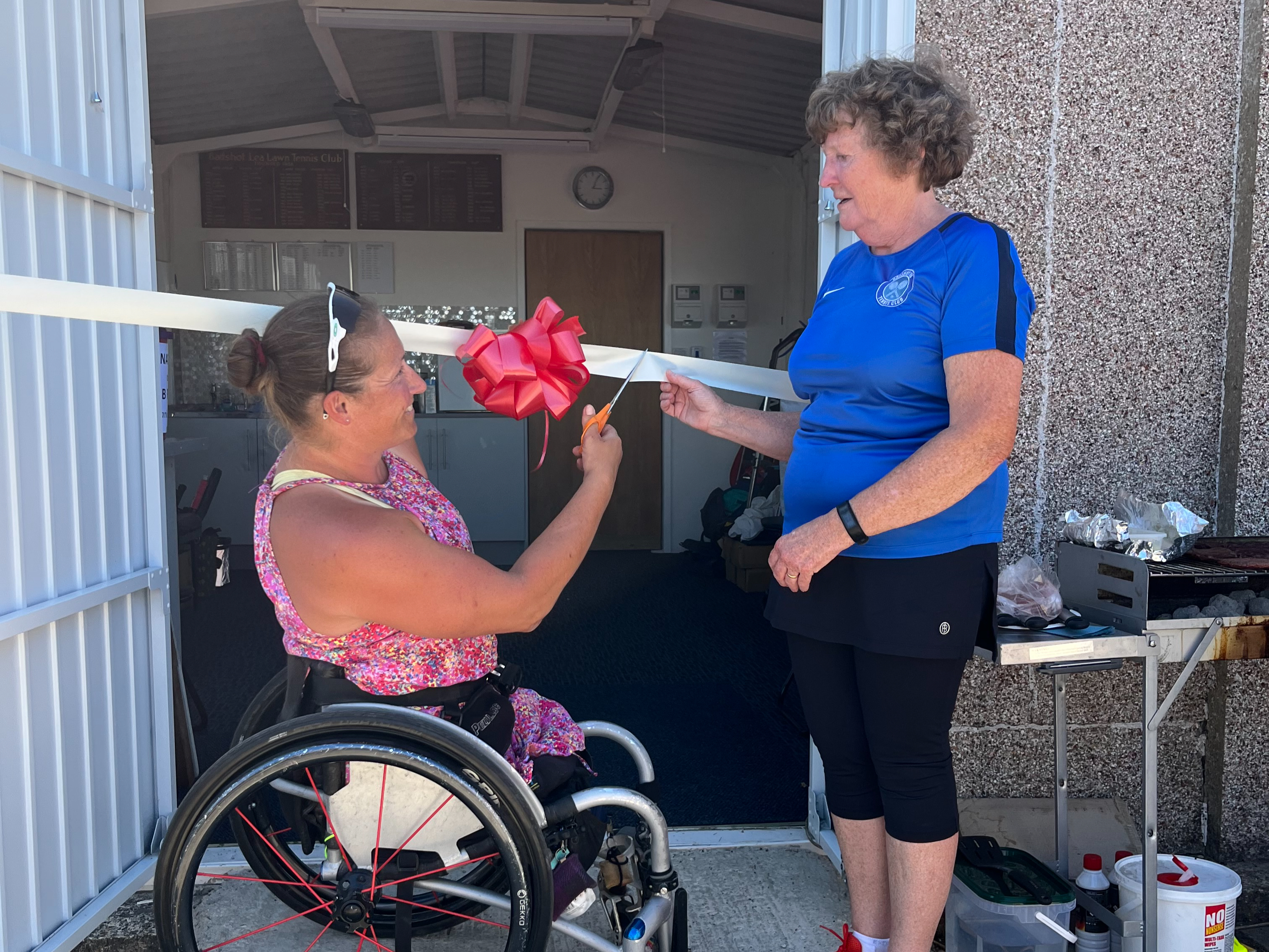 <p>Paralympian Rachel Morris cuts the ribbon to open Badshot Lea Tennis Club’s floodlights and new accessible facilities chair, watched by club chair Gillian Hyman</p>
