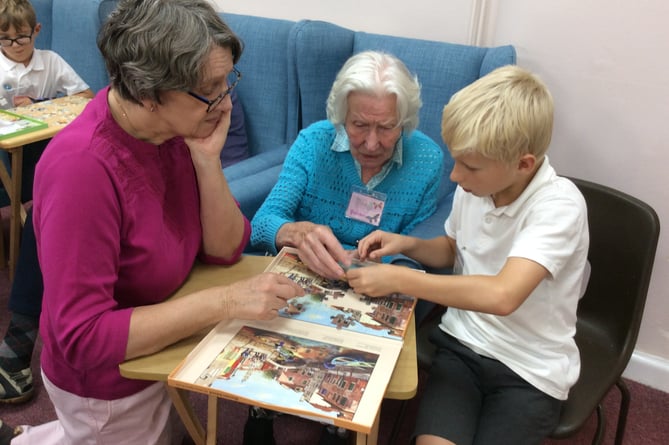 A pupil from St Lawrence CE Primary School in Alton does a jigsaw puzzle with two visitors to The Dementia Café in Alton Community Centre, November 2022.