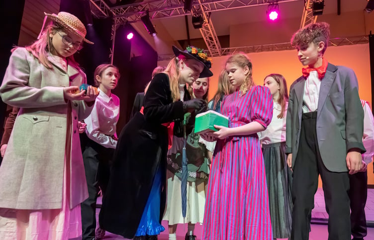 Mrs Corry (Siena Phipps) showing Mary Poppins her box of words. With them is Bert and Jane Banks.