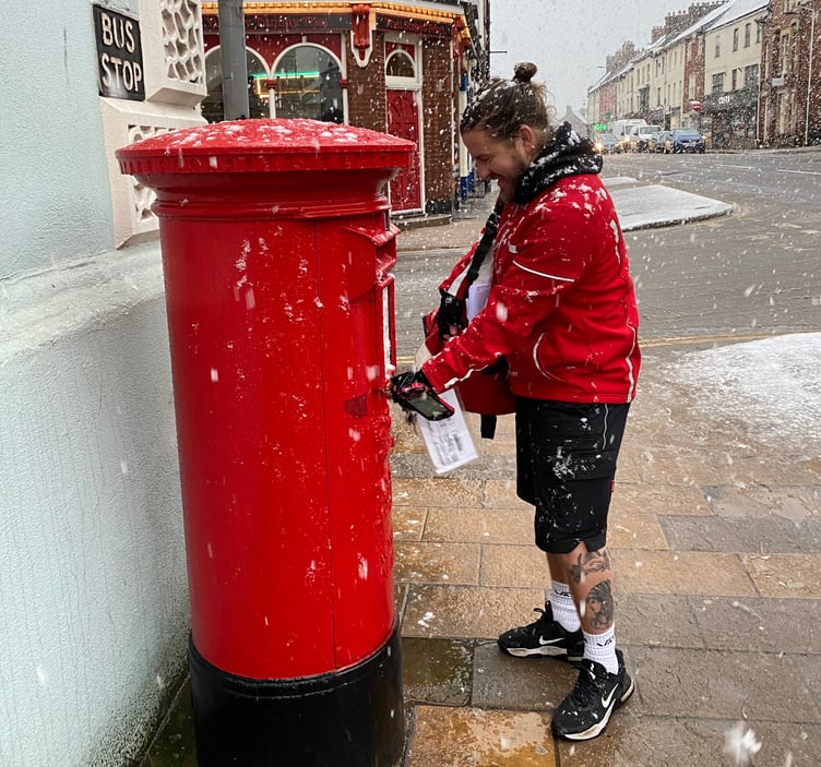 A local postman emptying the post box on Crediton High Street in a snow shower.