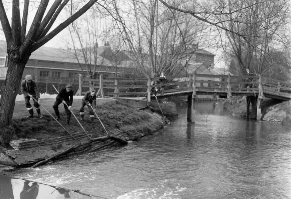 <p>Workmen from the Thames Water Board clear branches from the River Wey as it passes through Gostrey Meadow, Farnham, in the spring of 1953</p>