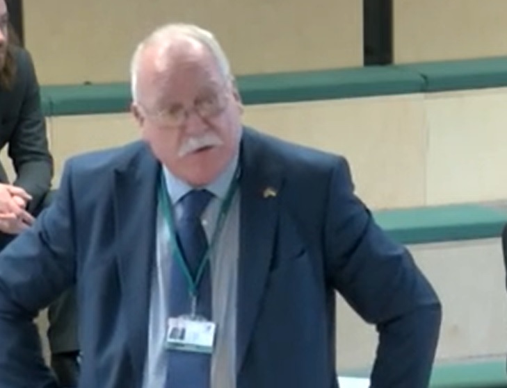 <p>Surrey County Councillor Trefor Hogg reading the imagined letter at a meeting of the council. Screengrab from meeting stream</p>