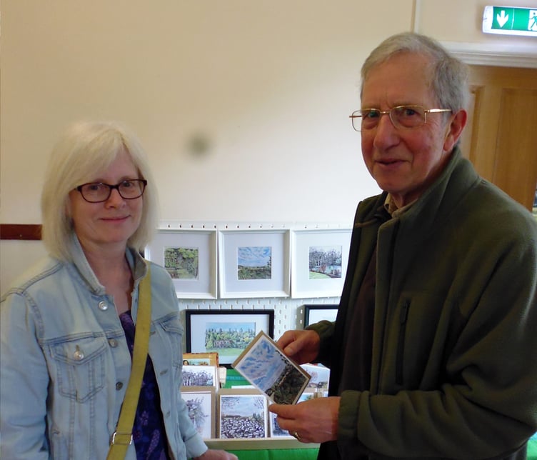 Carrie Clark showing her water colour paintings and cards of the village to customer John Wilson.