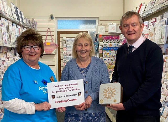 Hazel Evely, Crediton Morrisons Community Champion, left, and Alan Quick, Editor, ‘Crediton Courier’, right, present a Highly Commended certificate and tin of biscuits to Gail Wills, proprietor, Crediton Card Centre. NP 160523 03