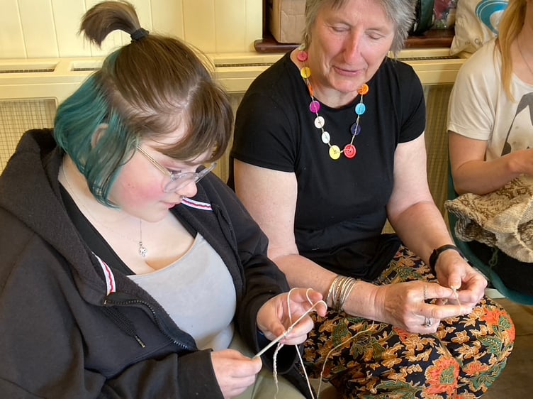 Caroline Ward teaching a young volunteer, Ray, how to crochet.