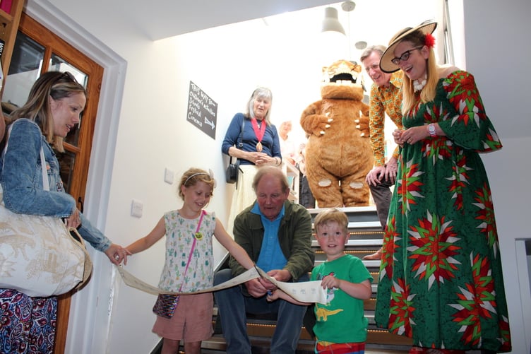 Ready to cut the ribbon is three years-old Quinton Cook, helped by eight years-old Cora Whitehouse with Michael Morpurgo and behind, Crediton Mayor Cllr Elizabeth Brookes-Hocking, the Gruffalo, Philip Reeve and Sarah McIntyre on the steps leading up to the extension. SR 8092