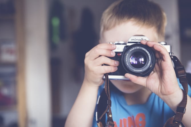 A young boy taking a photograph with an old SLR camera
