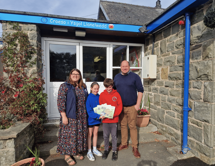 Sian Healey presenting the "Dan Y Bont" book Series to pupils and Mr Adam Shearman, Headteacher at Llanelwedd Church in Wales Primary School following giving a presentation to pupils launching the books on World Mental Health Awareness Day.