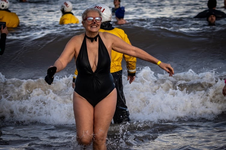 A woman in fancy dress smiles as she leaves the water after her dip.