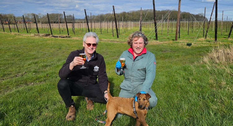 Hogs Back Brewery managing director Rupert Thompson (left) and hop garden manager Matthew King toast the brewery’s shortlisting in the SIBA Sustainable Business Award, accompanied by brewery dog Basil