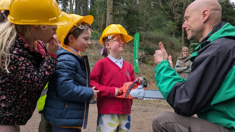 Young people are shown how to safely hold a chainsaw with this model.