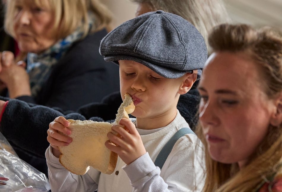 <p>A child in 1940s attire tucks into a slice of bread during a VE Day lunch in Binsted.</p>