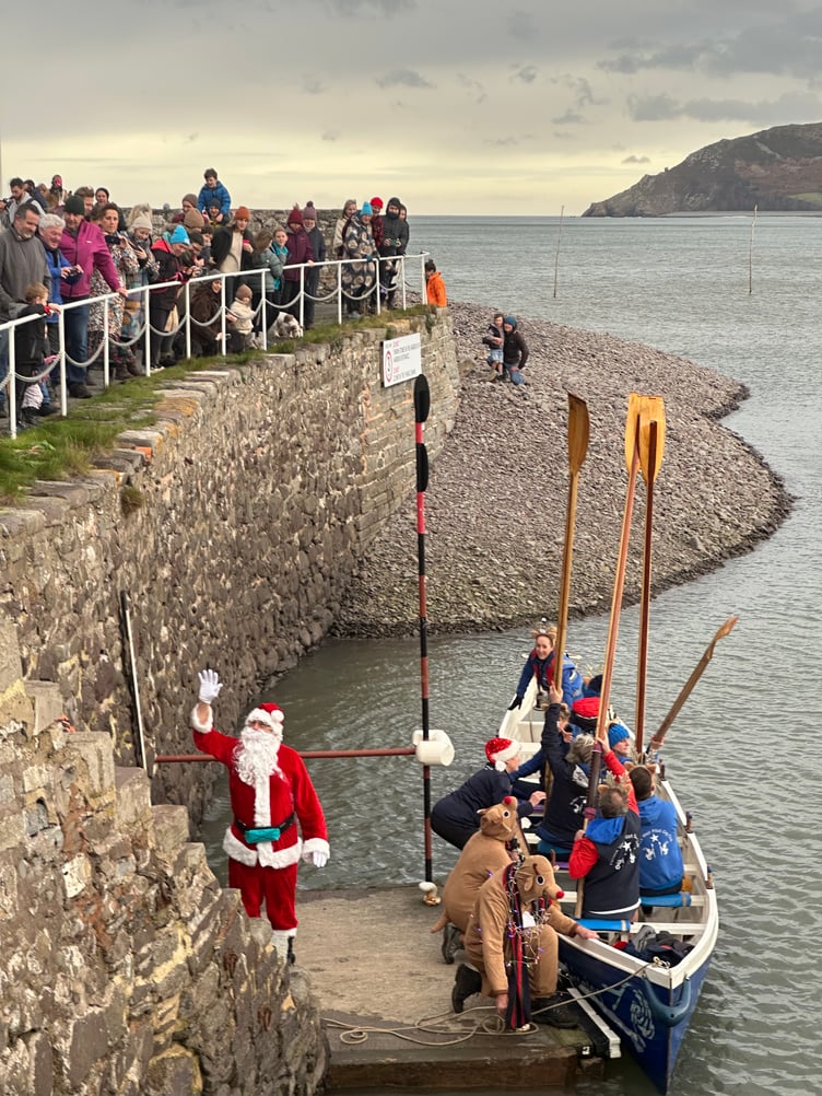 Santa alights in Porlock Weir harbour after being rowed in by gig club members.