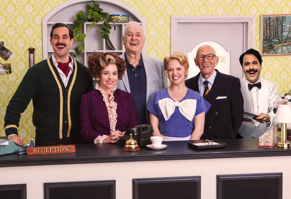<p>Behind the reception desk at Fawlty Towers, from left, are Danny Bayne, Mia Austen, John Cleese, Joanne Clifton, Paul Nicholas and Hemi Yeroham (Photo: Trevor Leighton).</p>